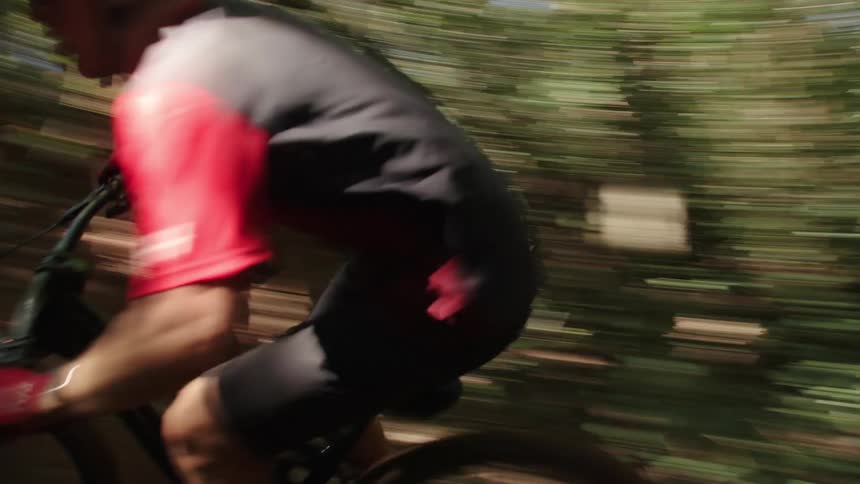 A teenager on a mountain bike is riding fast around an embankment in the woods