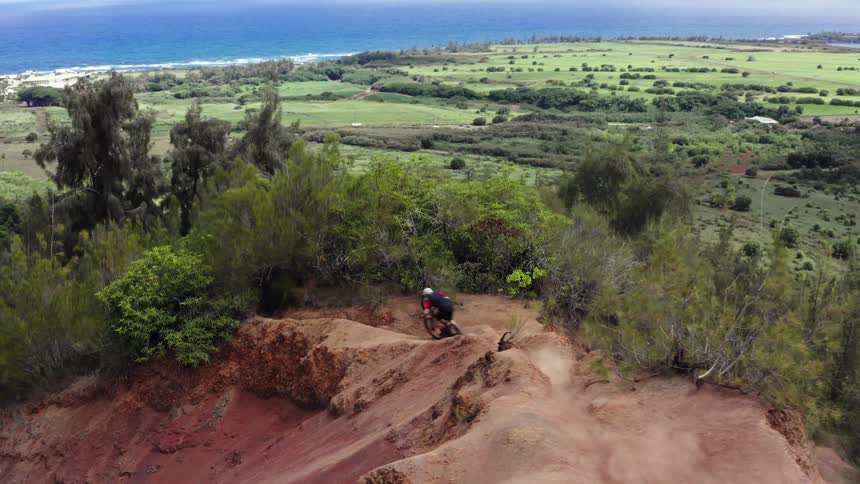 Cyclist rides over trail along ridge overlooking land leading to water and nearby town