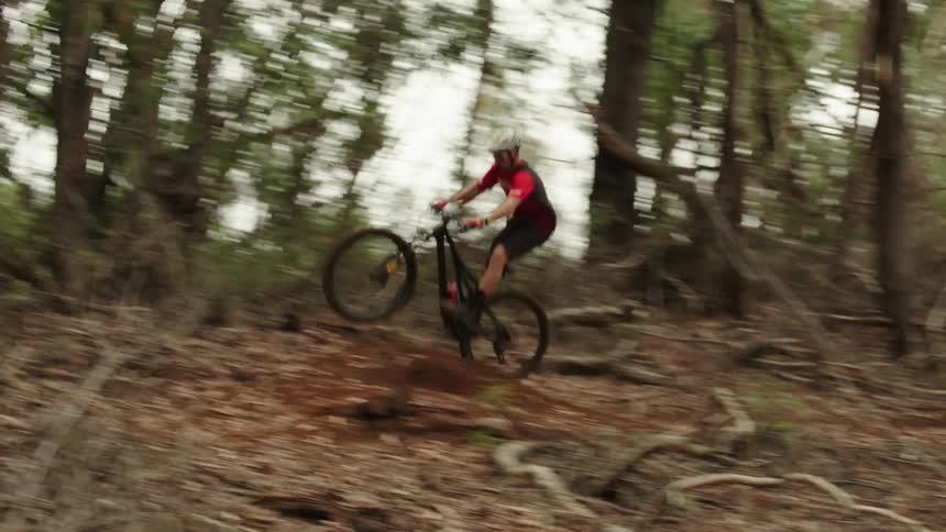 A man going over a jump on a mountain bike in a forest
