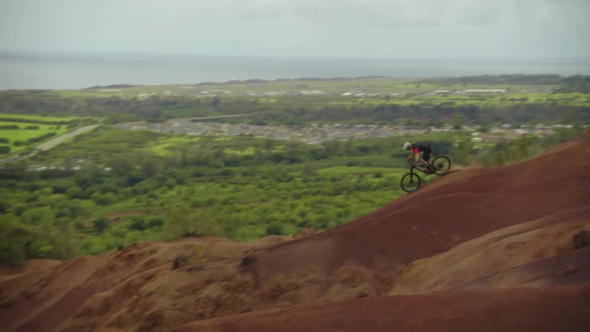 Cyclist rides dirt bike down dirt slope with town and lake in the background