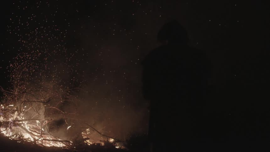 A man stands by a burning fire at night