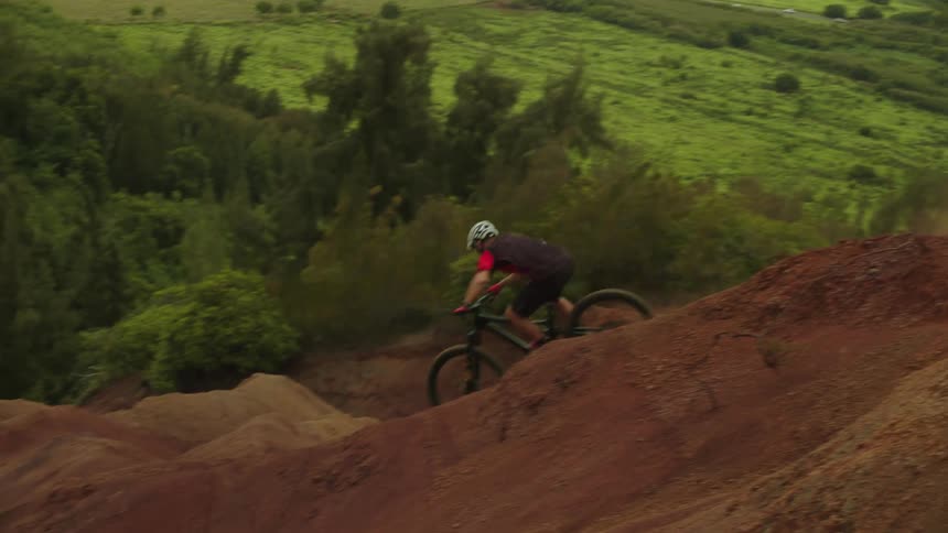 A cyclist rides down dirt hills near a open field