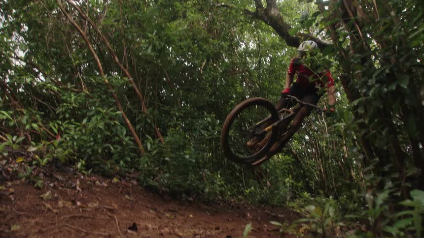 A man on his bicycle jumps in the air while riding down a dirt path in the woods