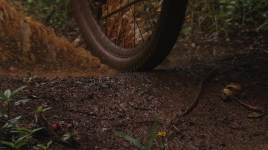 A cyclist gets caked in mud after riding through a puddle on a dirt trail