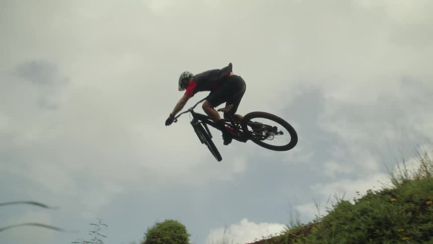 A boy on a bicycle rides up a hill and leaps into the air and turns the bike before he lands