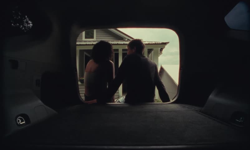 Young couple sitting on the back of a truck looking at a home while talking