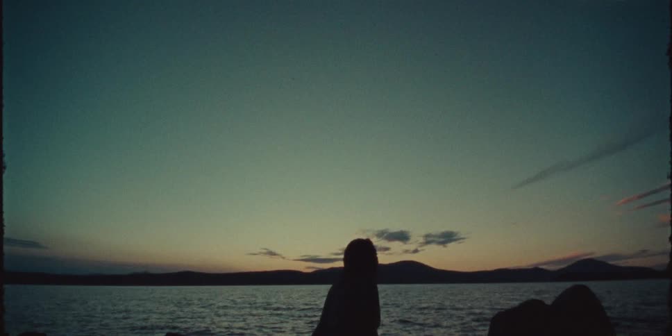 A person is sitting at the beach while the sun is setting