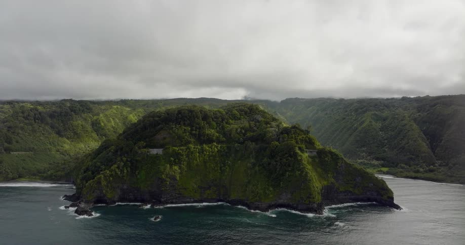 A mountain covered in greenery in the middle of a lake is shown with lush green mountains all over in the background