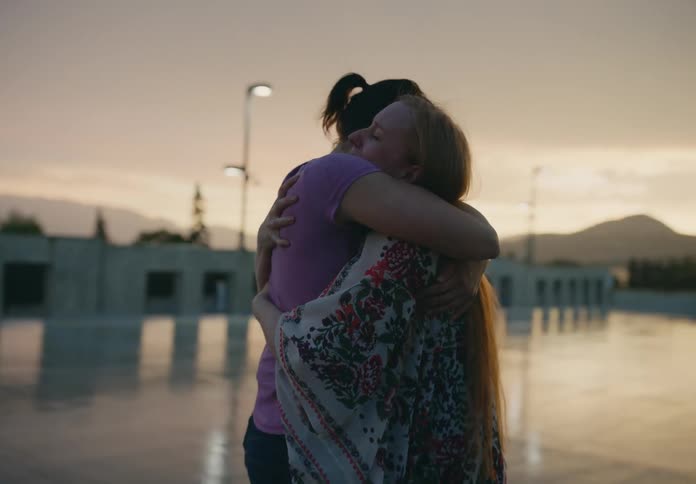Two women rush toward each other then smile and hug in parking lot with mountains on the horizon