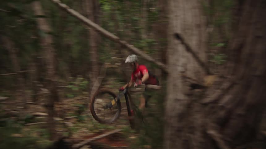 Man drives a motocross bicycle on a trail downhill through a forest at daytime