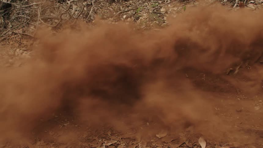 Dust flies in the air as a teenager rides a bike around a curve on a dirt trail