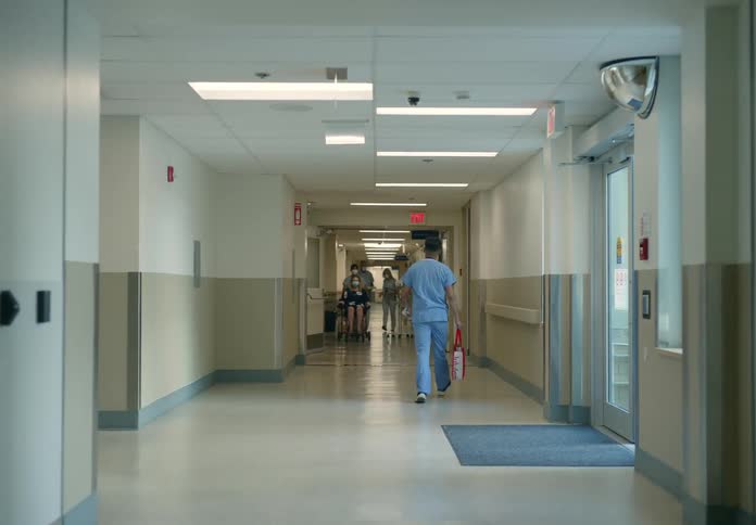 A corridor in a hospital with nurses wheeling patients in wheelchairs and people walking