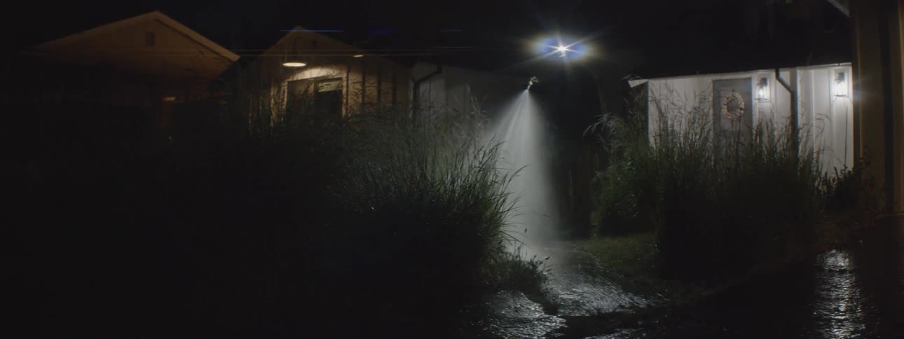 Man wearing headlamp waters plants in yard at night with a water hose