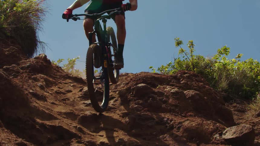 A man on his mountain bike rides down a very bumpy rock covered dirt slope in slow motion