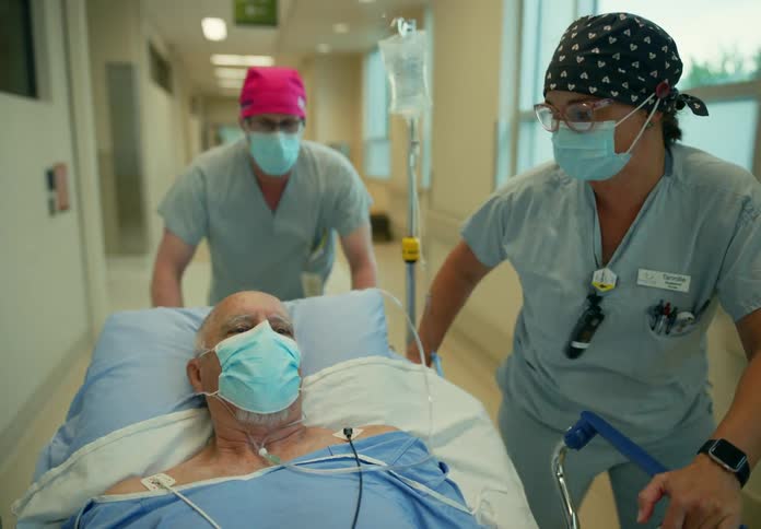 Medical personnel guide hospital gurney along hospital corridors