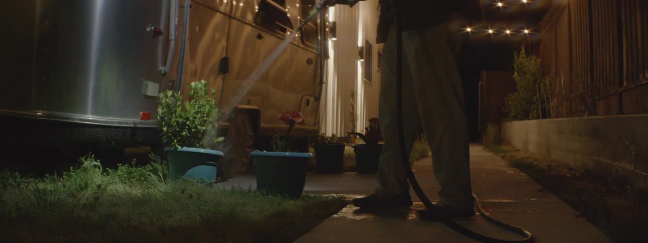 Man watering potted plants with a hose near his trailer at night