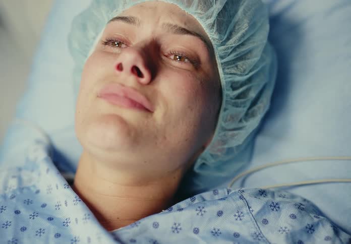 A woman patient is lying in a hospital bed upset and crying