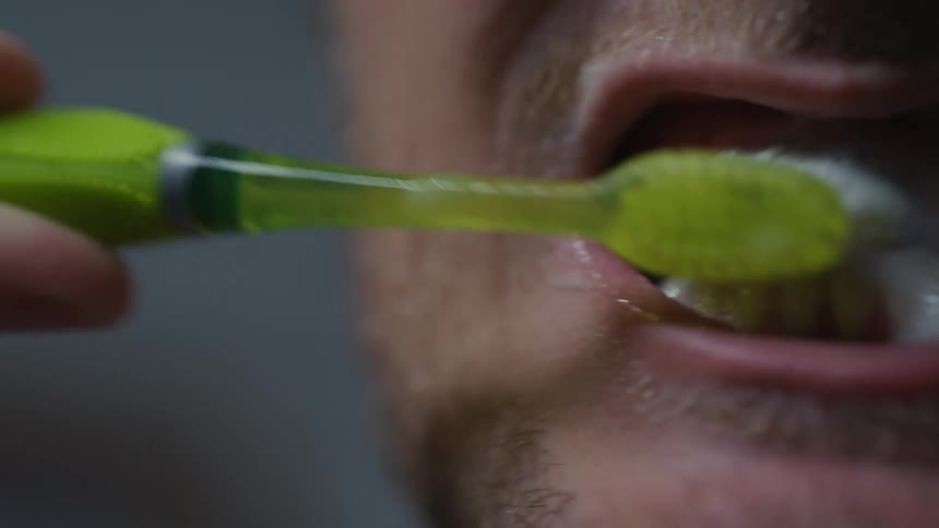 A man brushing his teeth with a green toothbrush