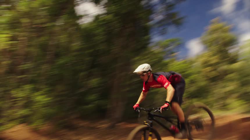 Cyclist takes jump at top of dirt slope before driving along dirt kickingup dust