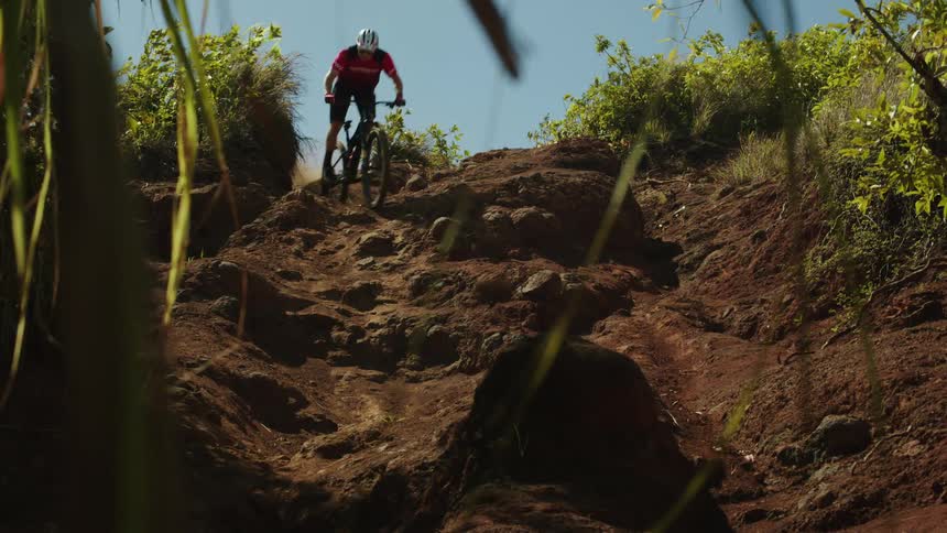 A teenage boy on a bike rides down rocky a dirt hill on a mountain bike leaping on his way down