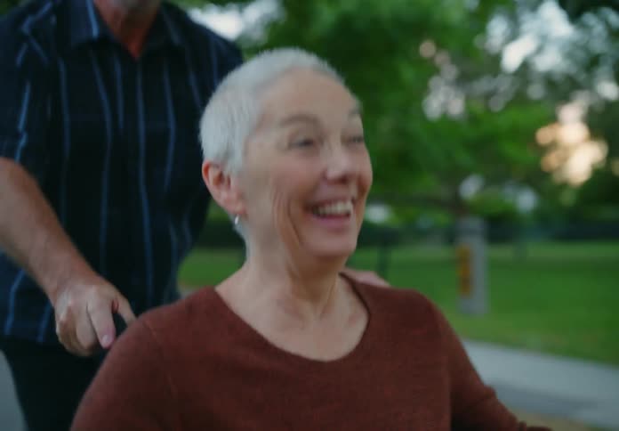 A woman laughs as a man running pushes her in a wheelchair