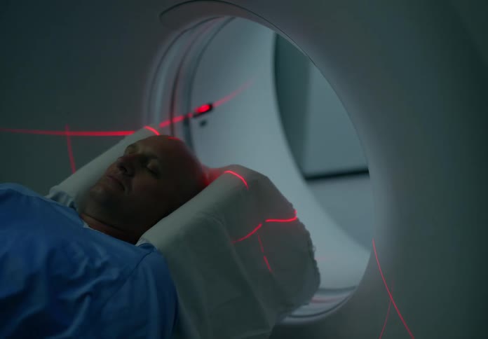 Red lights glow across a patients head and chest as he goes through a ct scan ring