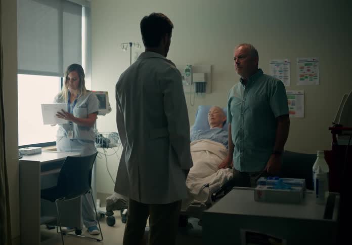 Doctor enters a room to talk to the companion of a man resting on a hospital bed