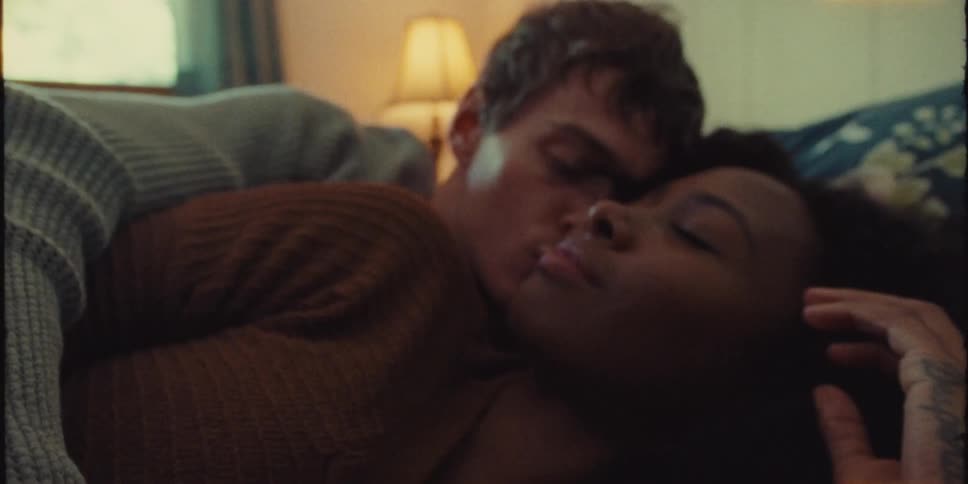 A young woman rests in the embrace of a young man on bed indoors during the day