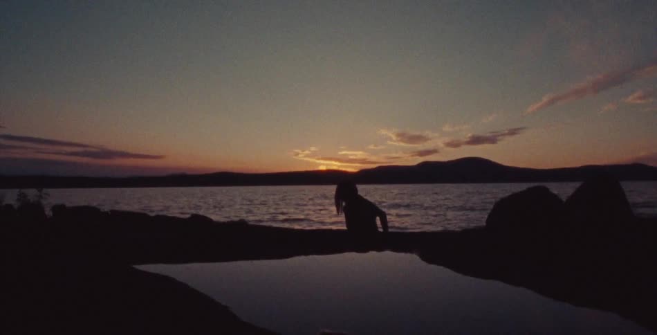 A woman crawling out of the ocean onto a beach at dusk