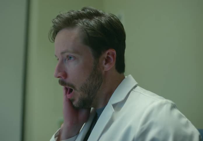 Doctor wearing lab coat working while sitting on a chair in an office yawning and then standing up