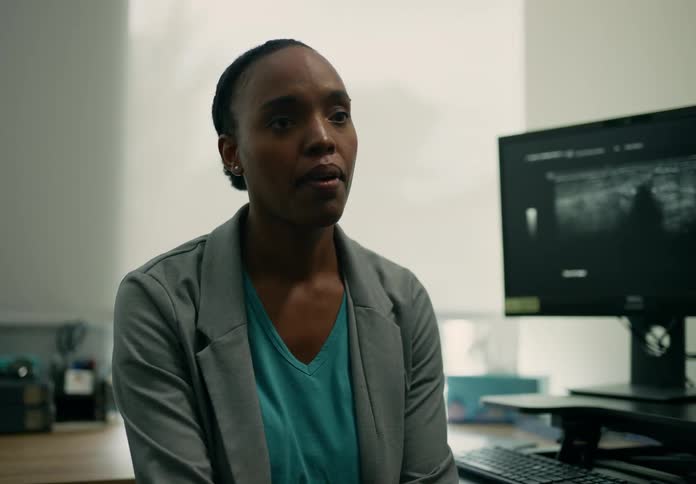 A hospital receptionist is sitting behind a desk with a computer as she speaks to someone