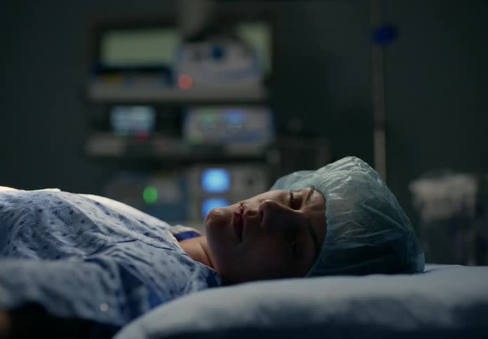 A woman patient is lying in a hospital bed looking scared and upset