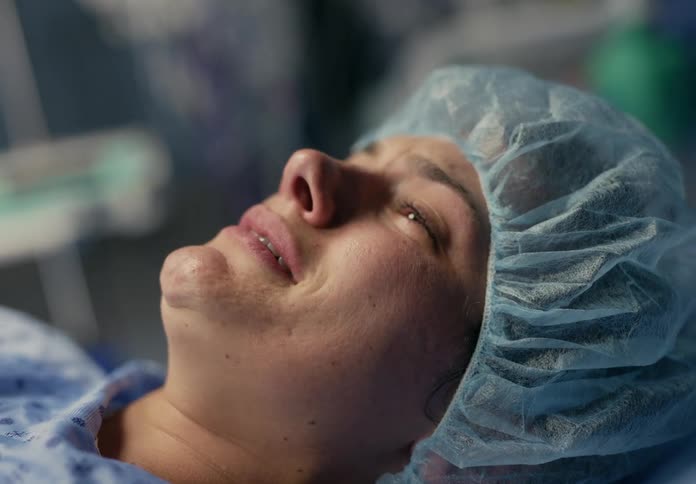 Scared woman wearing a hospital gown and cap crying while laying on a hospital bed
