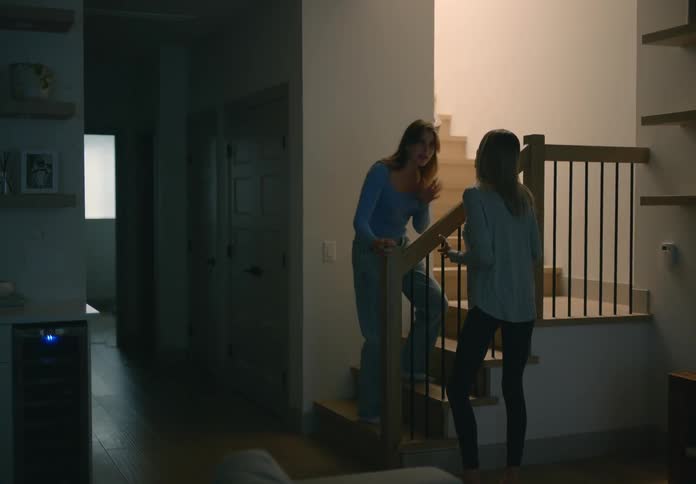 A teenage girl is arguing with her mother and she goes up the stairs as her mother has her hand on the rail looking up