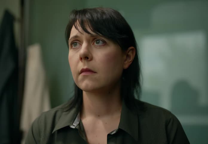 A woman is standing in a room looking around with a worried look on her face