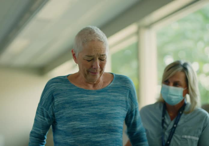 A nurse stands next to an elderly woman and encourages her as she walks in therapy