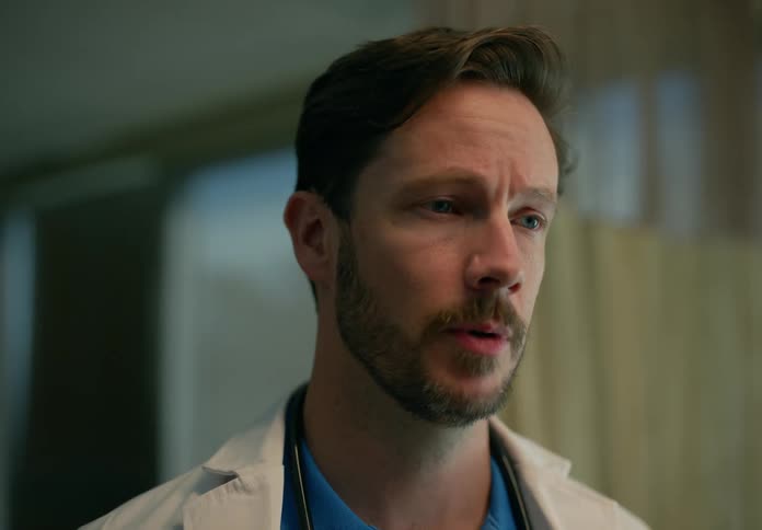 Male doctor wearing a white coat stands in hospital talking to patient