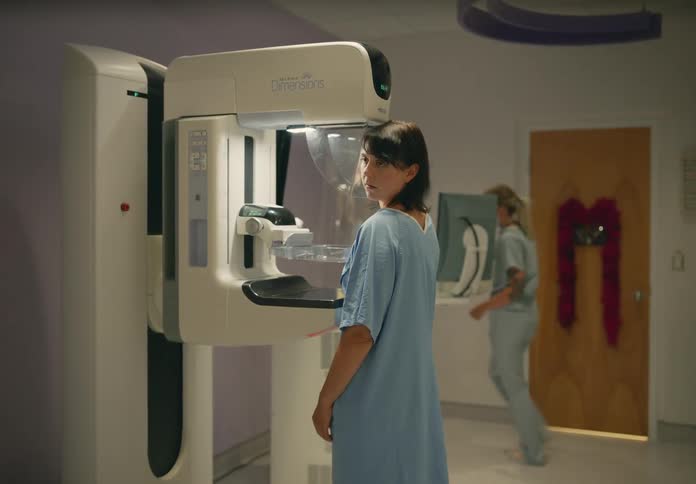 A technician places a woman in a machine and walks away to take the picture
