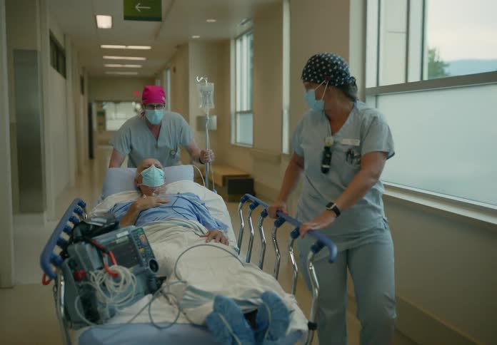 Medical personnel move patient in hospital bed along corridor