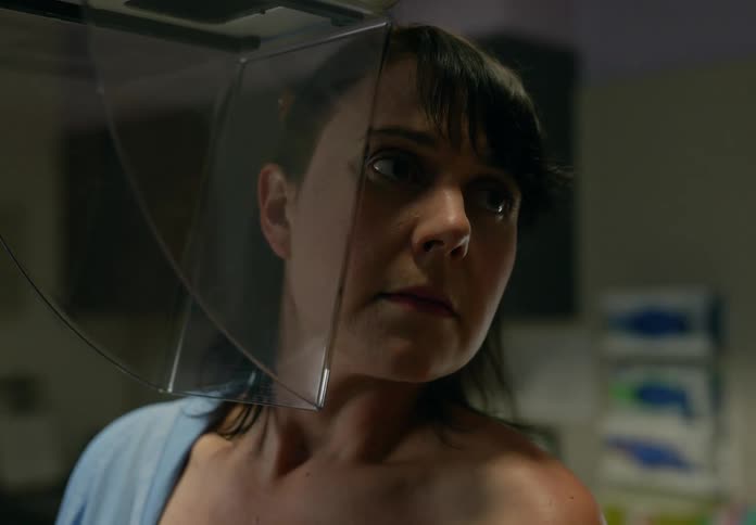 Technician helps a female patient to stand with her face pressed against a plastic plate
