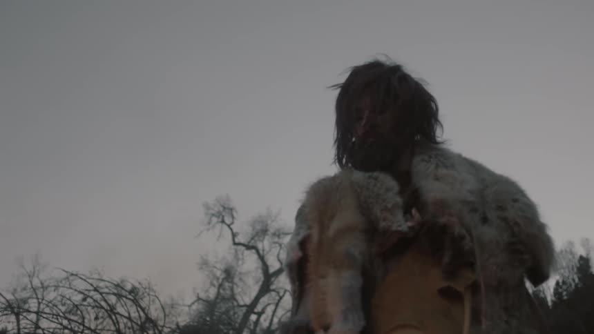 A man wearing furs around his shoulders looks down