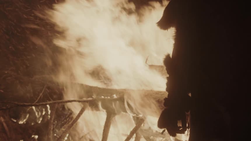 A man stands in front of a bonfire