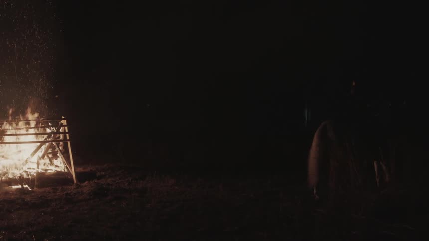 A person rides a horse away from a structure of wood slats that is burning