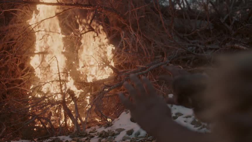 A man holds his hands out to be warmed by a pile of burning branches