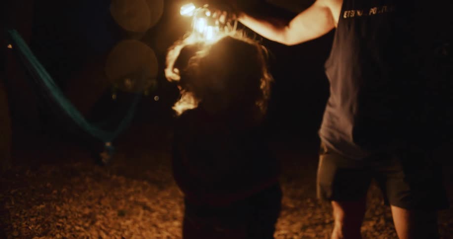 A girl helps her father untangle string lights in a barn