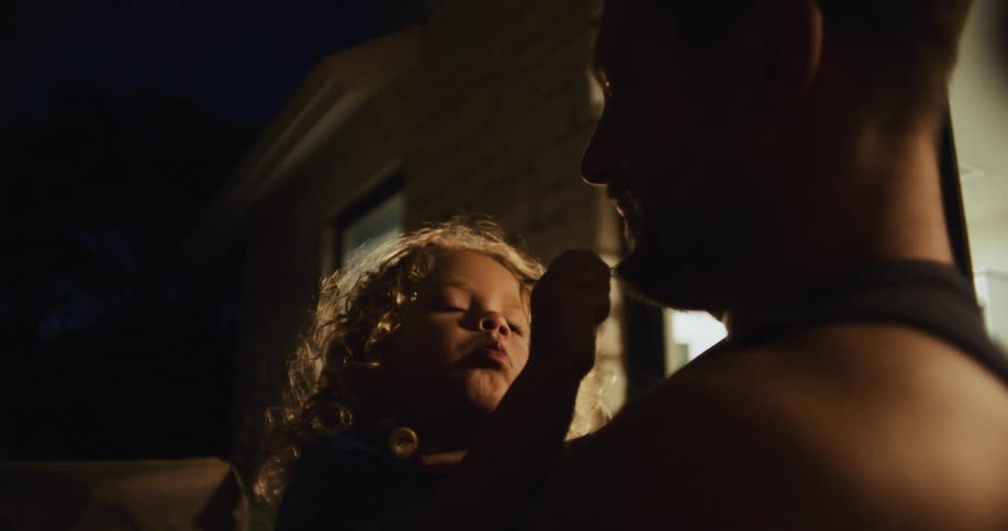 Daughter plays with the stubble on his father chin on the backyard at night