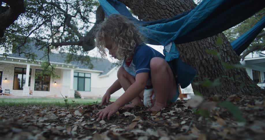 Blonde child plays in dirt near hammock hung on tree in backyard