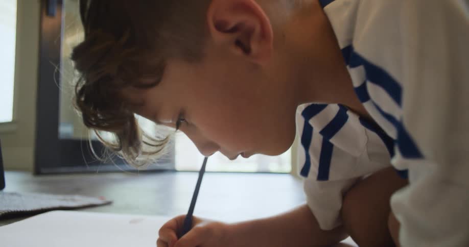 A boy draws while on the floor of his kitchen