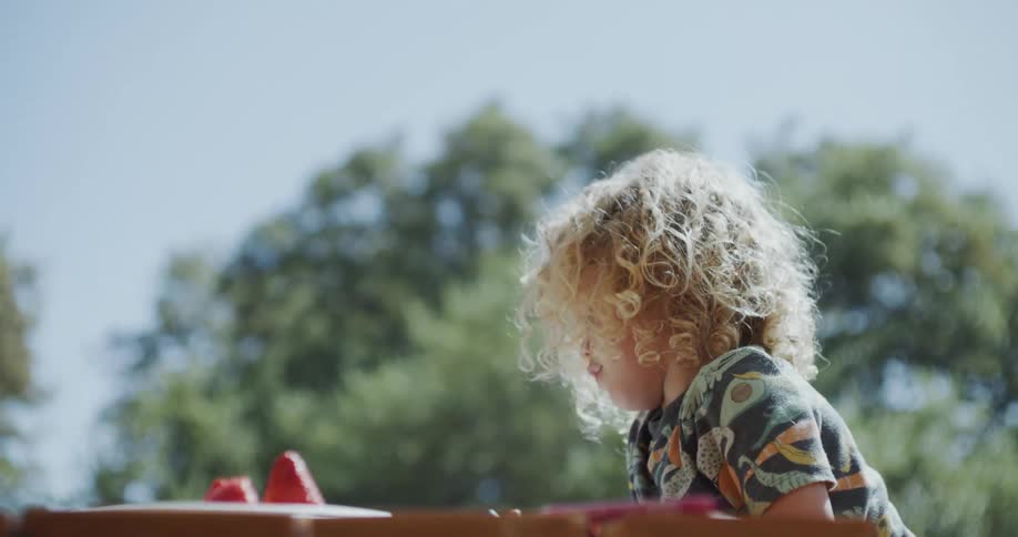 A young boy sits outside on picnic bench and colors