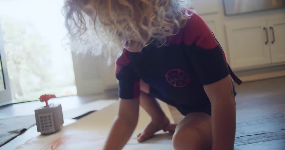 A little girl is sitting on the floor drawing on a sheet of paper with a pencil